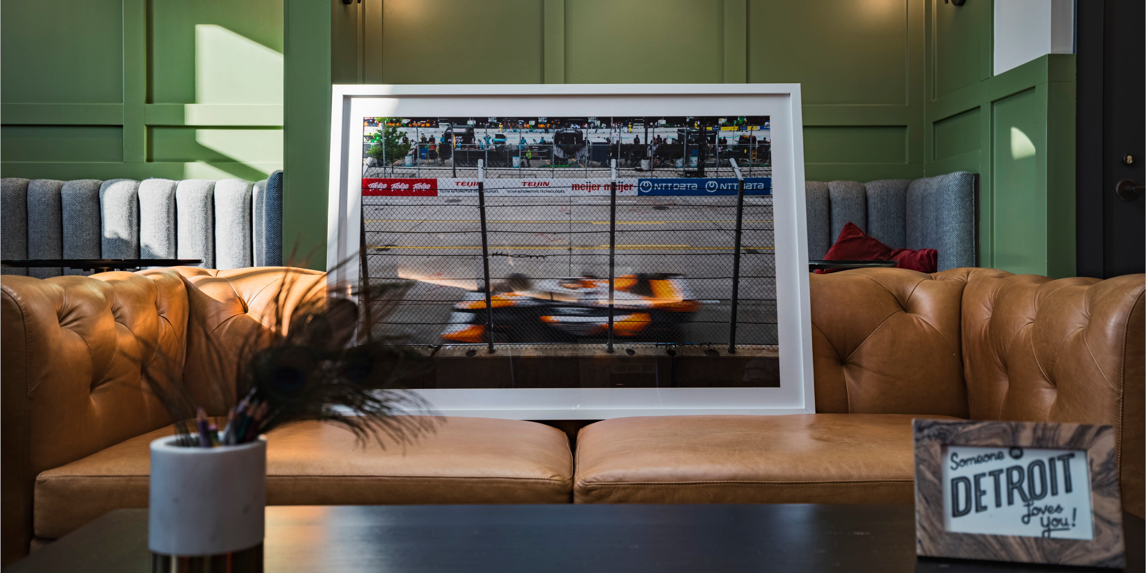 Framed picture of a race track on a brown leather couch with green walls.